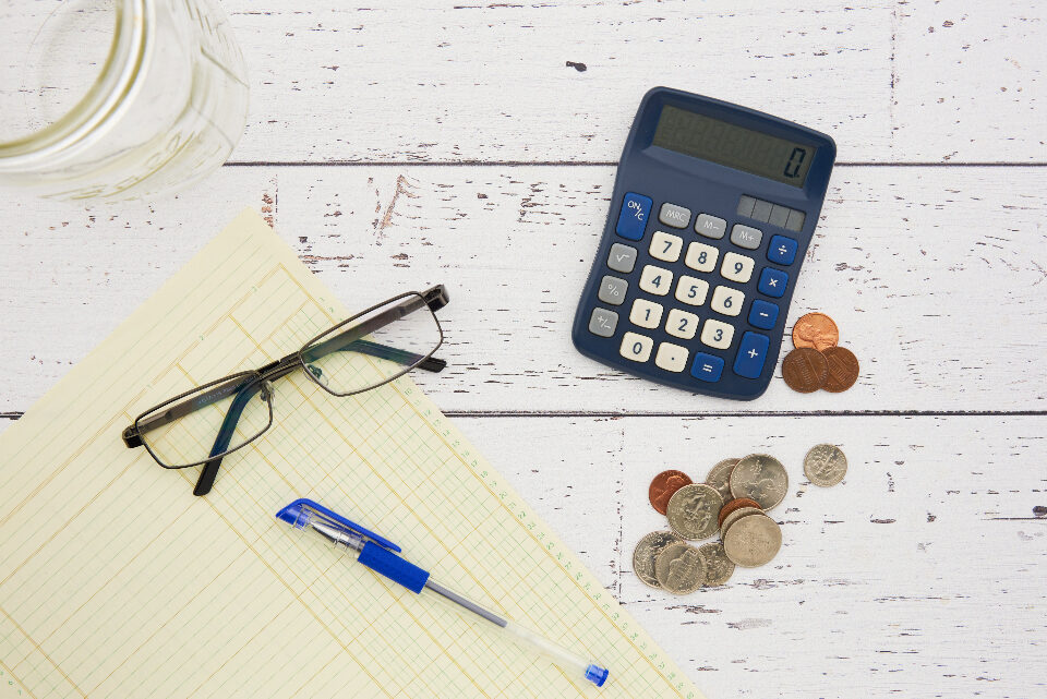 A calculator, a notepad, glasses and loose change on a desk