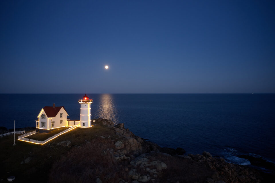 A lighthouse lit up at night under a full moon